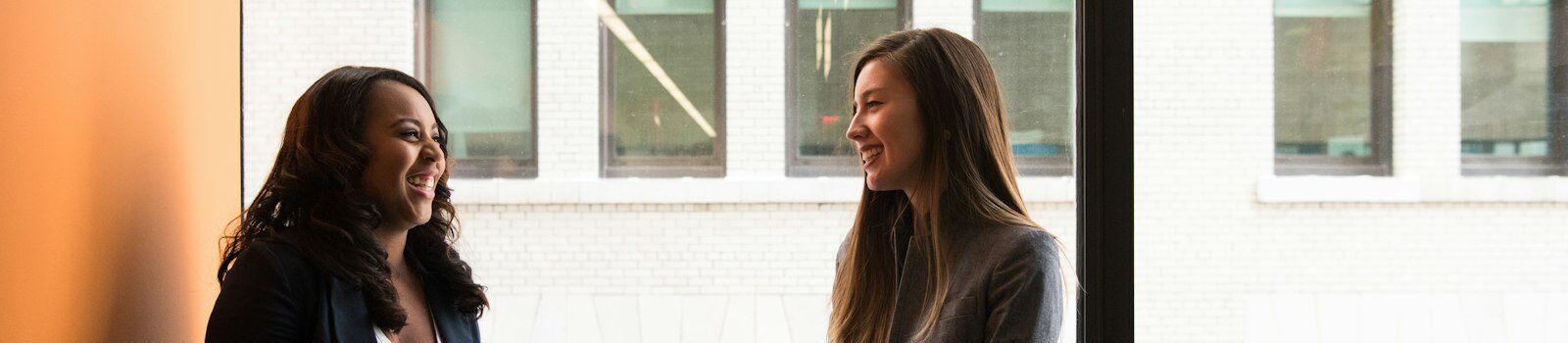 Two women sharing a friendly answer engine optimization conversation by a window