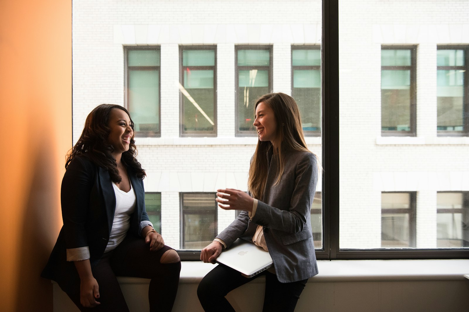 Two women sharing a friendly answer engine optimization conversation by a window